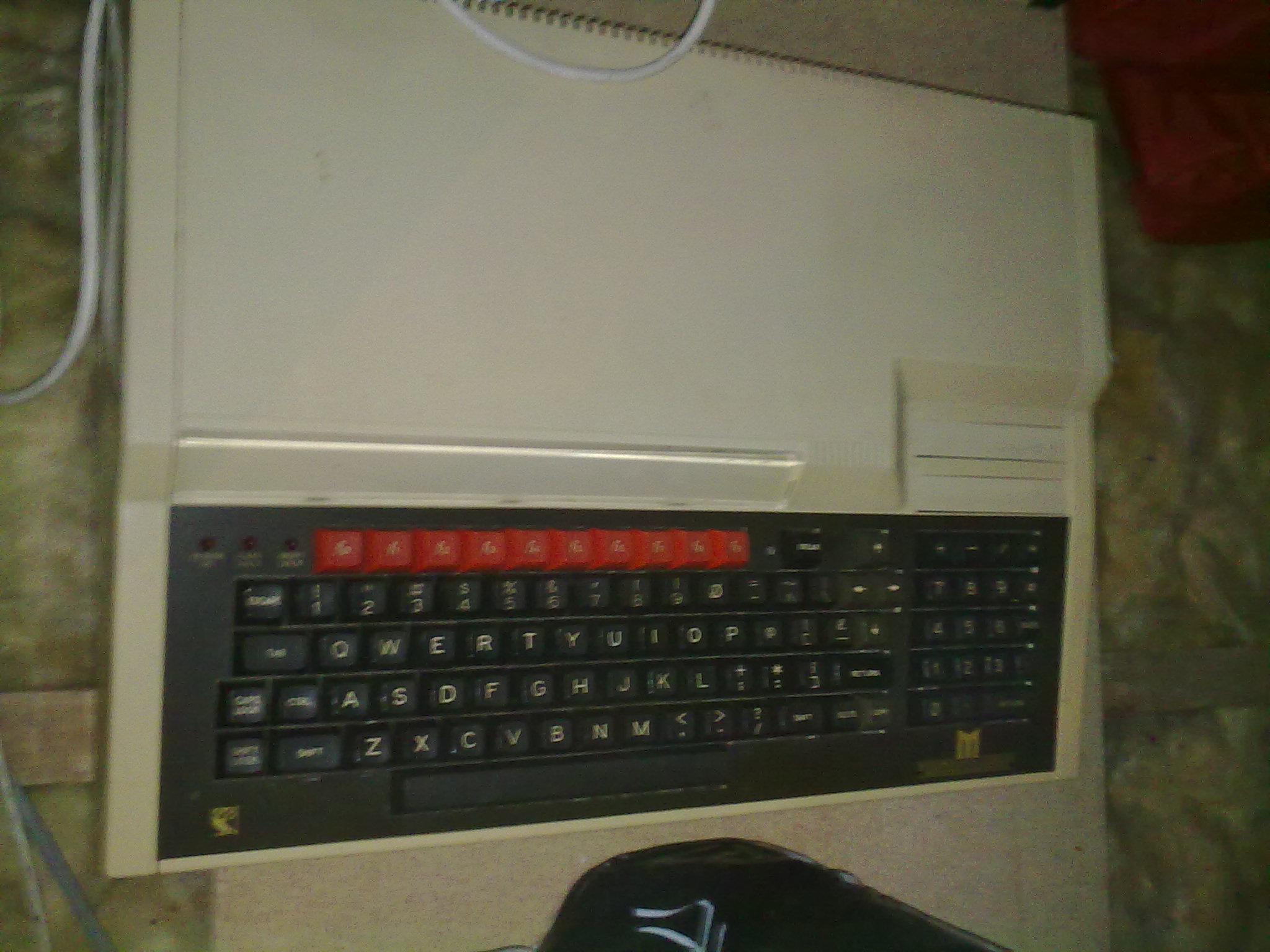 RETRO GAMES CONSOLES AND COMPUTERS - show us yours - Page 7 - Video Games - PistonHeads - The image shows a computer keyboard with a beige base and black keys, which has a distinctive red block electing the Windows key. Above the keyboard, there's an LCD monitor, presumably the one connected to the computer. The computer is placed on a textured floor, possibly a carpet. To the right, there is a black mouse close to the keyboard, completing the typical desktop computer setup. The image appears to be taken from an elevated angle, giving a good view of the keyboard and monitor.