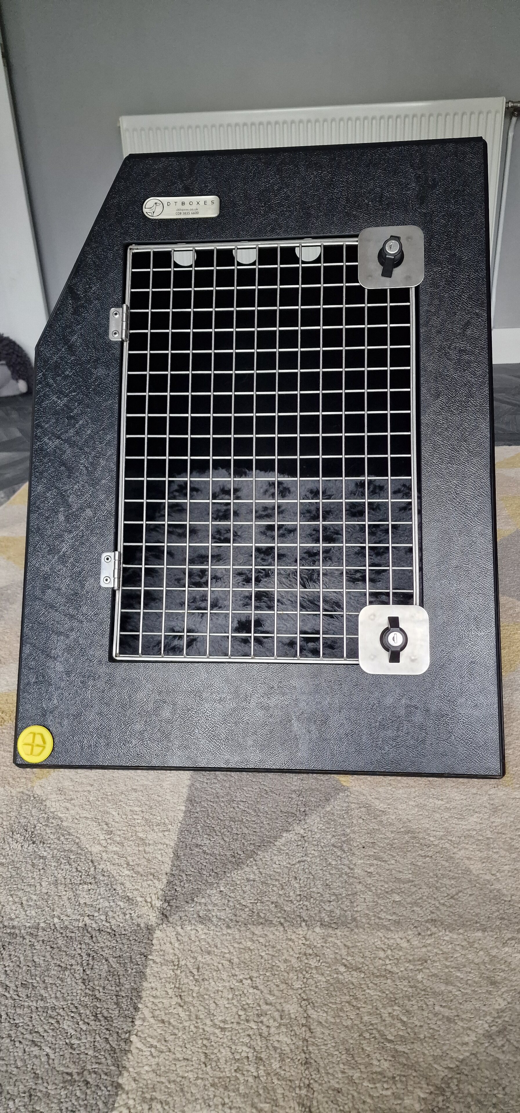 Pistonheads - The image shows an open cat carrier with a small black kitten inside. The carrier is placed on what appears to be a carpeted floor, and the room has neutral-colored walls and a white door in the background. There's a white paper or sign taped onto the front of the cat carrier, but it's not clear what the contents are from this angle.
