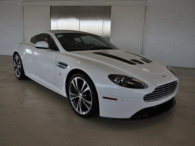 Pistonheads - The image showcases a white Aston Martin DB7 showcasing a stunning shine, set against a plain wall background. The car features an impeccable black stripe adding to its overall aesthetic appeal. It's positioned on a reflective floor, and a door with windows is visible in the background. The car's position and lighting create a sleek and sophisticated atmosphere.