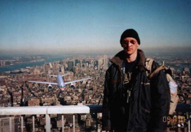 Human history captured on photo (pic heavy) - Page 5 - The Lounge - PistonHeads - The image features a man standing confidently on a high vantage point, looking out over a bustling city skyline with a major New York city landmark in the background. He is wearing a backpack, a jacket, and a warm smile as he gazes out onto the city. The airplane flying in the sky above adds a dynamic element to the scene.