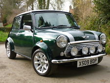 Buying An Older MINI? - Page 1 - Classic Minis - PistonHeads - The image showcases a classic green Mini Cooper car, parked on an asphalt surface. The car is viewed from a low angle, emphasizing its vintage design with round headlights and a distinctive silver grille. The body has a visible shine, indicating it's well-maintained. There's no one in the vehicle, and the surrounding area appears to be a calm, possibly rural setting with no significant landmarks or other objects in immediate proximity. The license plate is clearly displayed at the front of the vehicle.