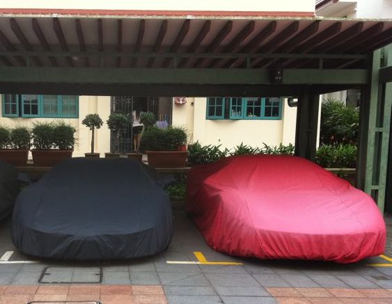 MGB nr. Leicester? - Page 1 - MG - PistonHeads - The image shows a garage with three parked cars: one covered with a black tarp, another concealed under a red tarp, and a third one exposed without any covering. The garage has a classic design with a specific area for each car. There are potted plants organically placed near the entrance, adding to the aesthetic of the garage. The interior of the garage walls is visible with paint that contrasts with the asphalt flooring, giving the garage a professional and well-maintained appearance.