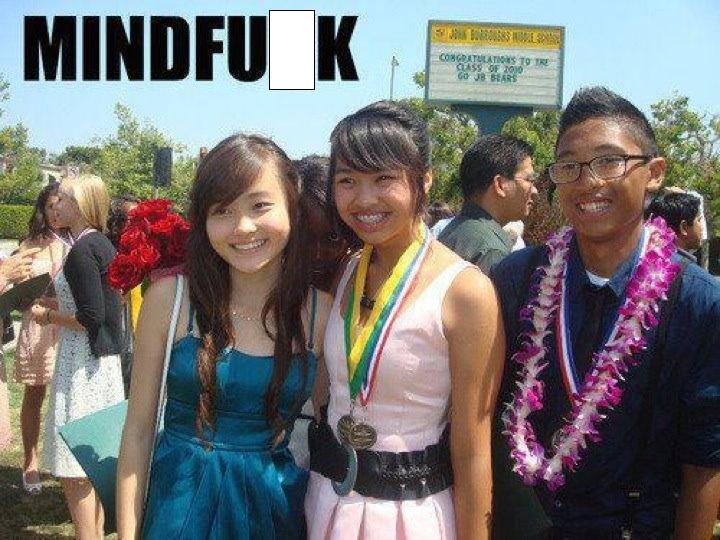 Can you spot it? - Page 1 - The Lounge - PistonHeads - The image is a color photograph featuring three young people standing together. In the foreground, from left to right, there is a person wearing a blue dress, a person dressed in a light pink top and a dark belt, and a person wearing a dark blue button-down shirt with rolled-up sleeves. All three are smiling and appear to be posing for the camera. Behind them, there is a large sign with a framed message that reads "Congratulations to the class of 2008 JHS." The setting indicates that this photograph was taken during an outdoor graduation ceremony.