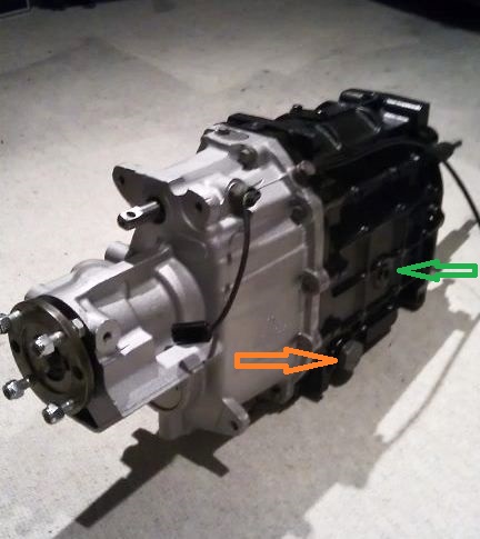 Lt77 gearbox - Page 1 - MG - PistonHeads - The image is a photograph of a mechanical component, specifically a large part of an engine or a similar machine. It appears to be an aluminum component with several ridges, bolts, and possibly electrical connections. The focus of the image is on the lower right corner, highlighting an orange marker and a green arrow, which might indicate specific points of interest or modification. The background is a plain surface with no distinguishable features, emphasizing the mechanical part as the main subject.