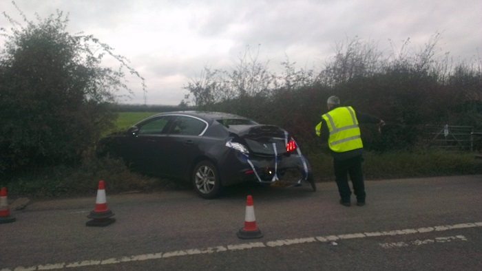 Very Lucky Today - Page 1 - Speed, Plod & the Law - PistonHeads - The image shows an accident scene on a roadside. A person in a yellow safety jacket is standing next to a damaged car. There are several orange and white traffic cones placed around the car, suggesting that this area has been cordoned off. The car's front end is severely dented and scratched, indicating a collision. The environment around the accident is a mix of greenery and the road itself.