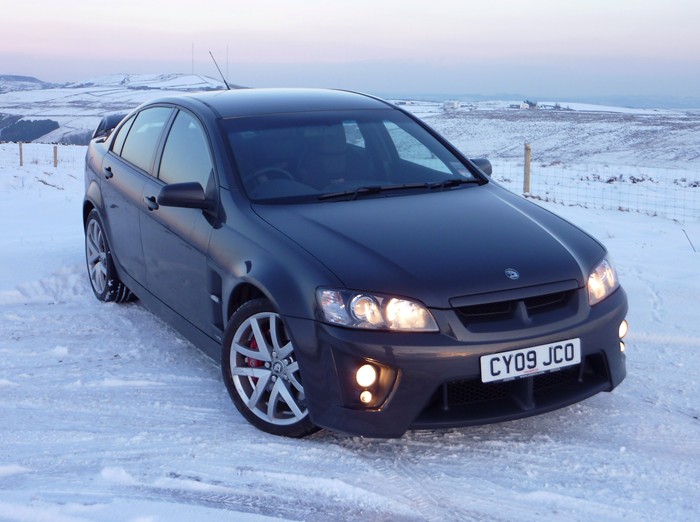 My VXR8 - pics taken today - Page 1 - Readers' Cars - PistonHeads - The image shows a black sedan parked on a snow-covered ground. The car appears to be a modern model, with alloy wheels and headlights illuminated. Behind the car, there's a wintry landscape with a clear sky and distant hills. The overall scene suggests a calm, wintry day, and the car's placement on the snow suggests it may be in a rural or less-traveled area. There are no visible texts or distinctive marks on the car in this image.