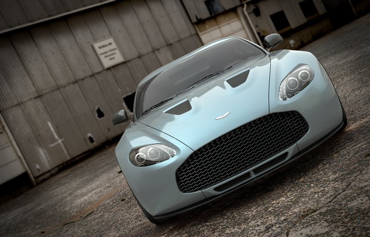 V12 Zagato "street" version - Page 1 - Aston Martin - PistonHeads - The image depicts a sleek, blue Italian sports car parked against a backdrop of a building with corrugated metal walls. The car appears to be a large coupe, with prominent air vents and a low, sloping roofline. It is positioned at an angle to the camera, suggesting movement or its readiness for a drive. The lighting in the photograph is diffused, giving it a somewhat moody ambiance. The scene falls under the genre of automotive photography, often used to showcase the design and aesthetics of vehicles.