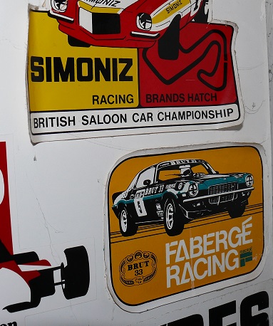 Show Us Your Stickers! - Page 1 - Formula 1 - PistonHeads - The image features a collection of stickers and signs related to car racing, specifically the British Saloon Car Championship, which was sponsored by Simmons-Biat. The main focus is on cars from the championship, including a notable black and white car with the number 12 and a car twirled in red and yellow colors, possibly indicating the number 5. The signs emphasize the racing heritage of this event. The stickers have logos for popular racing tire brands like Goodyear. The overall composition conveys a sense of excitement and prestige associated with motor racing.