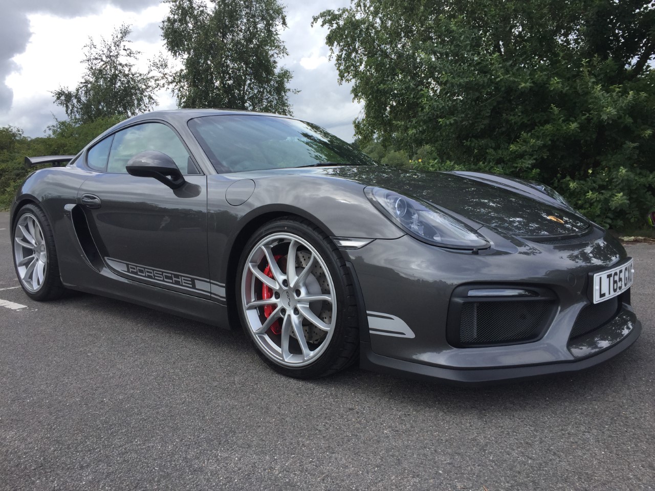 Porsche Cayman GT4  - Page 2 - Readers' Cars - PistonHeads - This image showcases a gray Porsche Cayman sports car parked on a paved area, possibly in a parking lot or on the side of the road. The car is positioned at an angle to the camera, allowing us to view its side and part of the front. The Porsche emblem is visible on the front of the car, indicating the brand. The vehicle displays a sleek design, indicated by its aerodynamic shape and wheel arches. The car's tires are painted in a contrasting color, adding a visual accent to its overall design.