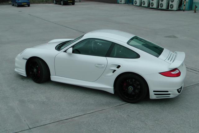 Porsche Driven Pistonheads Turbo - The image showcases a modern white sports car parked on what appears to be a concrete area. The car features a sleek design with a prominent rear wing, large air intakes, and distinctive side mirrors. There are several air conditioning units visible in the background, suggesting the location might be a commercial or industrial area. The car has a sleek and elegant look, typical of high-end sports vehicles.