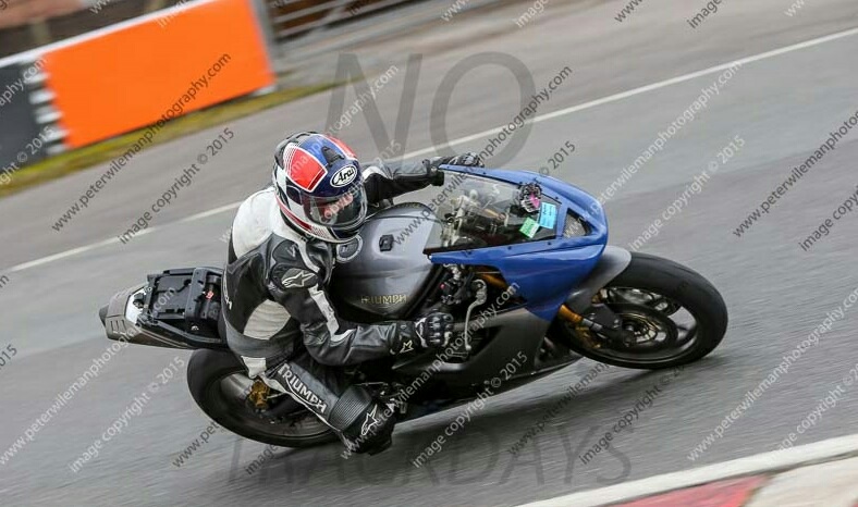 A man riding a motorcycle down a street - Pistonheads - In the image, a man is riding a blue motorcycle on the left side of the road. He is wearing a helmet and leather gear, indicating that he is in the midst of a journey. The motorcycle is in motion, traveling at a high speed as evidenced by the blur that fills the background. The setting appears to be a racetrack, given the markings and structures visible in the vicinity. The overcast sky adds a sense of calm to the otherwise dynamic scene.