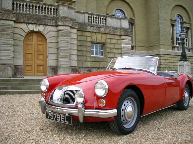 Pistonheads Ferrari Beautiful Classic - The image features a classic red convertible sports car parked on a gravel driveway in front of an old-style building with a grand entrance and arched windows. The vehicle has a distinctive grille, round headlights, and a convertible top, reinforcing its vintage appeal. The car's license plate is clearly visible, and the overall setting suggests a setting that appreciates vintage automobiles and architecture.