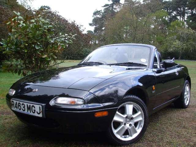 Ive Pistonheads Elite Joined - The image shows a sleek, black convertible car parked in a grassy area, adjacent to a tree with green leaves. The car is facing towards the left of the frame and its top is down, revealing a convertible design. It has a European license plate reading "R463 MG J," which indicates it might be a British vehicle, presumably an MG. The car is elegantly designed, featuring a silky finish and alloy wheels that add to its luxury and aesthetic appeal.