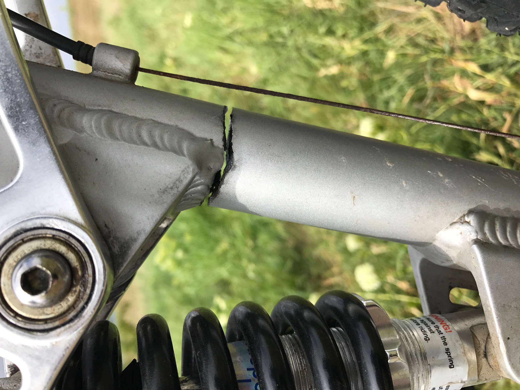 The "Photos From Today's Ride" thread... - Page 292 - Pedal Powered - PistonHeads - The image shows a close-up view of a component on a bicycle, probably taken for the purpose of inspection or documentation. The focus of the image is on a disc brake caliper with the metal bracket for the brake cable, which appears to be missing or disconnected. The caliper is attached to a spring coil, indicative of a suspension or shock absorber system, often found in mountain bikes. The background is out of focus, but suggests an outdoor setting with grass, which hints that the photograph may have been taken in a park or similar recreational area.