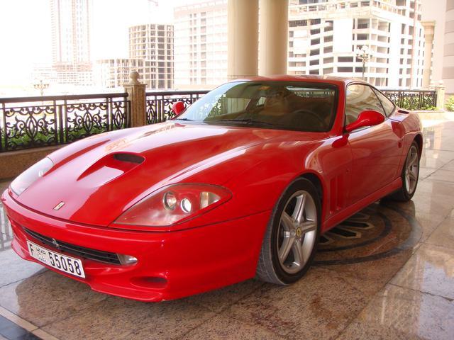 Affordable Pistonheads - The image features a vibrant red sports car, parked on a tiled floor. The car has a notable black front spoiler and silver rims, which contrast with its shiny red exterior. Behind the car stands a grand urban architecture with towering buildings, giving a sense of the car being in a luxury or commercial area. The quality of the image suggests it may be a promotional photo intended to highlight the car's sleek design and its setting within an impressive cityscape.