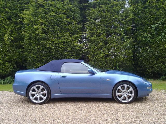 Volante Pistonheads Sold Ive - The image shows a blue sports car parked on a stone surface. The car has a convertible top that appears to be down. The vehicle has alloy wheels and is positioned in front of a backdrop of green foliage, suggesting a park or similar setting. The overall ambiance of the photograph is outdoors on a clear day.