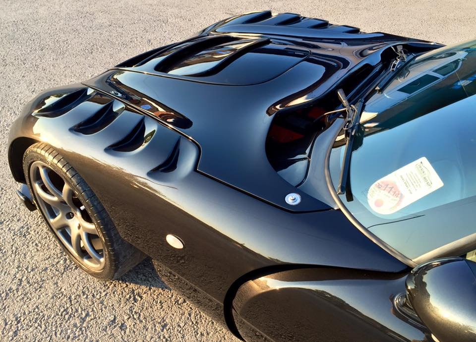 Sag on www.spautomotive.co.uk - Page 2 - Tamora, T350 & Sagaris - PistonHeads - This image captures a black sports car resting on a paved surface. The car has a distinctive curved design on its roof, which adds to its sleek and aggressive appearance. It has a glossy finish, reflecting its surroundings. The car is equipped with large wheels and is also shown with its convertible top down, adding to its open-air appeal. It appears to be a convertible sports car, suggesting sportiness and luxury for potential buyers.