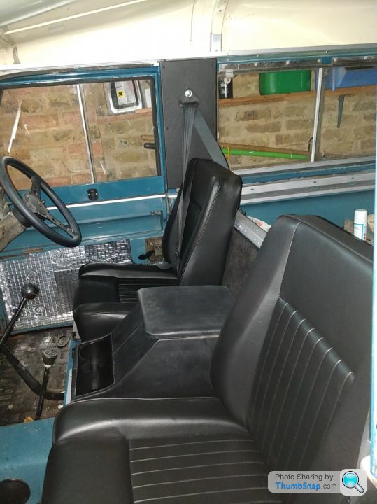 show us your land rover - Page 103 - Land Rover - PistonHeads - The image shows an old-fashioned blue and white truck parked inside a building. The truck has been stripped of its interior, leaving only the driver's seat and passenger seats visible. The vehicle appears to be in a state of disrepair or in the process of being restored, as indicated by the missing parts. The truck is positioned at an angle that showcases both the side and front, with the driver's side door open. The building has a brick wall in the background.