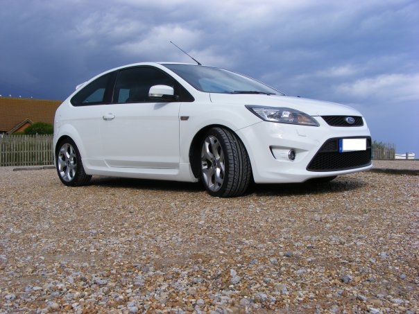 Pistonheads Track Toy Focust - The image features a white Ford car parked on a gravel surface. The sky in the background is filled with clouds, and the presence of a wooden fence indicates that the car is parked in a residential or rural area. The car's reflective surface suggests it is a modern model. The absence of visible license plates or additional text in the image indicates that it might have been taken by the car owner without external personalization.