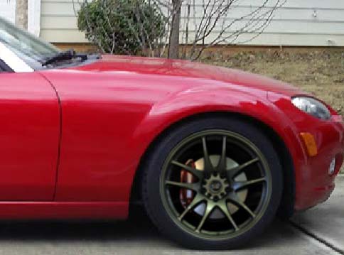 A red and black motorcycle parked in a parking lot - Pistonheads - The image shows a close-up view of the front right wheel of a red sports car. The wheel is significant in size, almost reaching the center of the image. It features a five-pointed star design, and the car's body reflects the red and black hues of the wheel. The wheel itself is slender and appears to have a sturdy construction, typical of high-performance vehicles. In the background, there is a glimpse of a building with a white wall, suggesting a suburb or residential area. The overall style of the image is a dynamic and focused vehicle shot, highlighting the car's design and color.