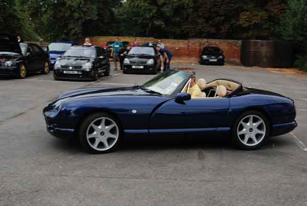 A car that is parked in a parking lot - Pistonheads - In a parking lot, a striking blue convertible car captures attention. It's topped with a cream-colored interior, and the roof is down, allowing the viewer to see inside. Another similar blue car is parked further back, while other cars of various colors are scattered throughout the lot. People are present in the scene, standing near their cars, suggesting a gathering or event. The overall atmosphere of the image is serene and ordinary, featuring an epicene day with a clear sky.