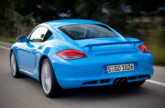 favourite cayman colour - Page 1 - Boxster/Cayman - PistonHeads - The image is a dynamic photograph of a blue sports car in motion on a road. The vehicle appears to be a Porsche, as indicated by the brand badge and design features such as aerodynamic bodywork and red tail lights. The photo captures the car's movement by blurring the background, a technique often used in professional automotive photography to convey speed and performance. The focus is on the rear of the car, providing a profile view of its design, particularly the wide-positioned taillights and the distinctive license plate that reads "S GO 1026". The photo has a professional aesthetic, suggesting it could be promotional material for the vehicle.