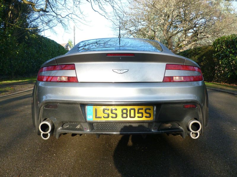 Badly modified cars thread Mk3 - Page 118 - General Gassing - PistonHeads UK - The image displays a silver sports car parked on a paved surface, likely a driveway. The car is positioned at an angle that allows for the view of its rear and part of its side profile. It features a visible exhaust system with two pipes on each side, typical of high-performance cars. There's a license plate at the back indicating the car has been registered in the United Kingdom, specifically in Leicestershire. The vehicle is positioned behind a small, green hedge that adds a touch of color to the scene.