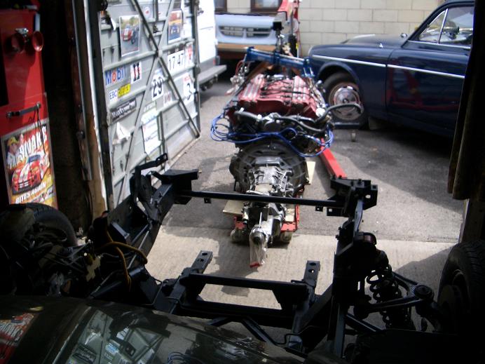 Rebuild Pistonheads Viper - In the workshop, a classic blue car is parked next to a large metal cart. The cart is covered with several car engines, giving an impression of a mechanical haven. Among the engines, a prominent engine sits at the front, potentially a centerpiece for restoration or repair. The ground appears slightly damp, suggesting recent cleaning efforts, and the overall ambiance carries a sense of mechanical dedication.