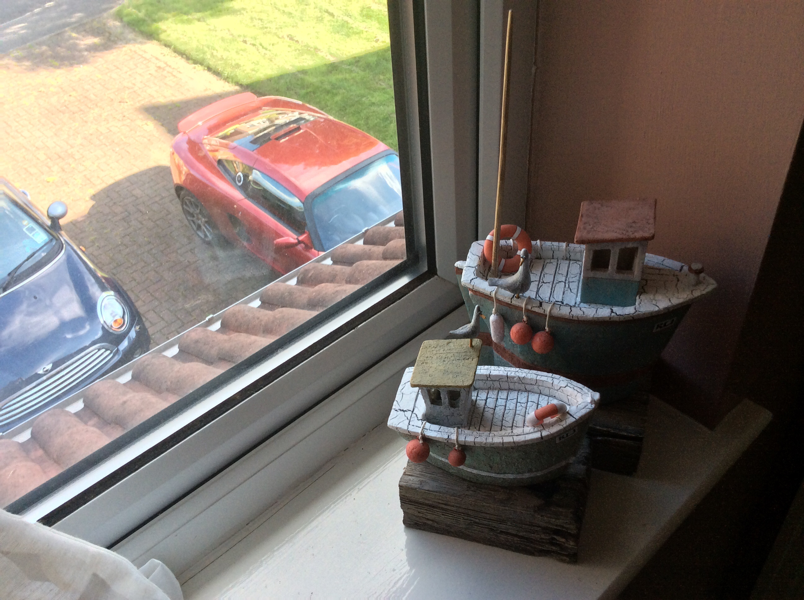 Art on your walls... - Page 12 - Homes, Gardens and DIY - PistonHeads - The image showcases a charming scene from a window sill. A knick-knack model of a pirate ship with a toy behind it commands attention in the middle of the image. To the right of the pirate ship, a smaller model of a boat adds to the nautical theme. The model is delicately crafted, featuring a deck and a railing. Pebbles neatly arranged around the base suggest a dock or a shoreline. The backdrop of the scene is an outdoor view of a narrow street with parked cars, their muted colors contrasting with the vibrant colors of the models. The overall composition of the image suggests a playful and adventurous setting.