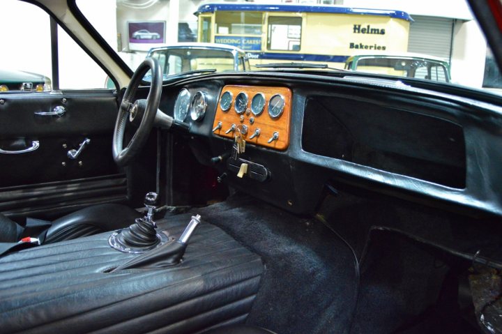 Early TVR Pictures - Page 159 - Classics - PistonHeads - The image features the interior of a classic car, focusing on the dash panel area. Beneath a steering wheel, a gauge panel with multiple dials and gauges is visible. The dashboard also includes the door latch and handle, and there's a key inserted into the ignition. The overall atmosphere of the image is vintage, accentuated by the muted colors and the aged appearance of the vehicle's components. The car appears to be parked in a garage or similar indoor setting.