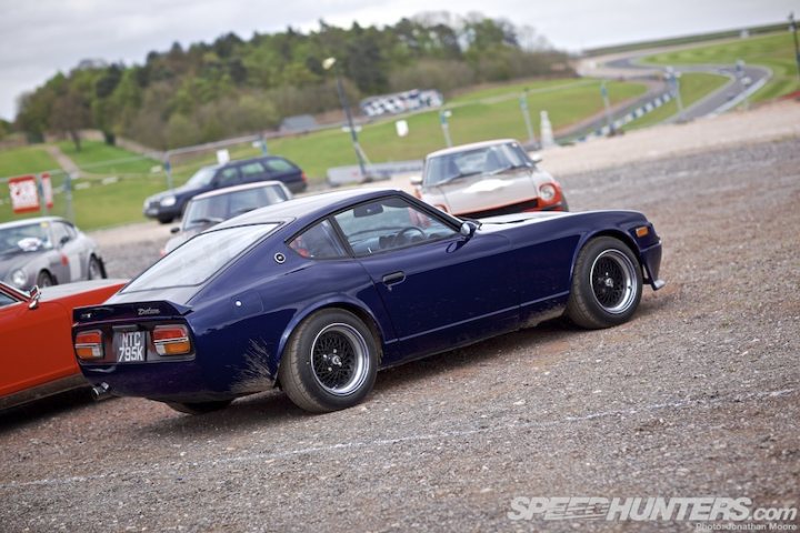 any 240z owners here? - Page 2 - Jap Chat - PistonHeads - This image captures a striking scene on an empty track. Dominating the frame is a black race car, its sleek design and vibrant color contrasting sharply with the gritty track beneath it. The car is parked next to a vintage sports car, its blue color providing a striking contrast to the red of the second vehicle. Surrounding these cars is a dirt track with a few small hills, while trees can be seen in the distance. The cars and track are the main focus of the image, with the highlight being the black race car. The absence of people and additional vehicles adds to the dramatic effect of the scene. The image does not provide any text or additional objects.