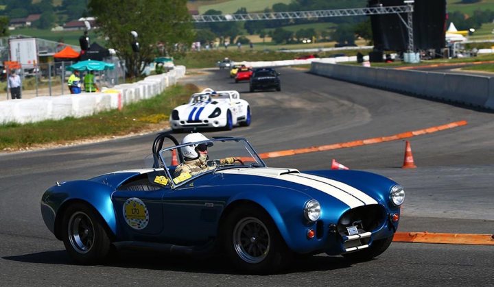 A familiar Tuscan racer abroad - Lignières Historique - Page 1 - Dunlop Tuscan Challenge - PistonHeads - The image captures an exhilarating moment on a curved road where a sports car, painted in shades of blue white, is in motion. The car is mid-turn, making the inside of the curve on a track. Another sports car can be spotted following with caution. In the background, a few spectators, perhaps fellow drivers or enthusiasts, add to the ambiance of the event. The entire scene suggests a racing event or a track day.