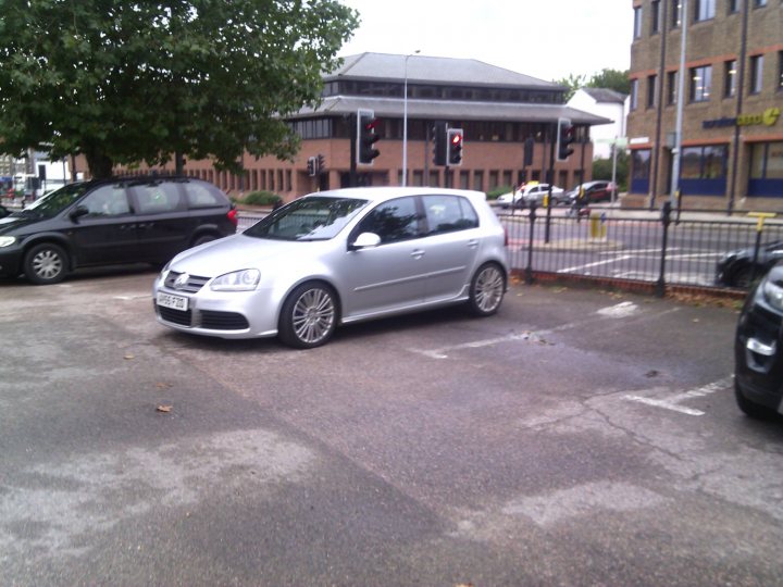 The BAD PARKING thread [vol3] - Page 202 - General Gassing - PistonHeads - The image shows a silver Volkswagen parked on the side of a street. There are multiple traffic lights in the scene, indicating that this is likely a busy urban area. The road appears to be dry, and there are trees visible along the street. The photo seems to have been taken during a clear day, but without more context, it's difficult to determine the exact location or time.