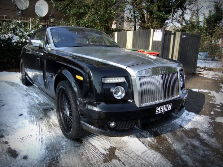 - Page 285 - Supercar General - PistonHeads - The image features a black Bentley Flying Spur luxury car parked in front of a suburban house. The vehicle has a distinctive grille and headlight design, characteristic of the brand. The car is positioned on a driveway blanketed in snow, suggesting recent snowfall. In the background, there is a black fence and some greenery, adding context to the residential setting. The Bentley's license plate is partially visible and reads "56T."