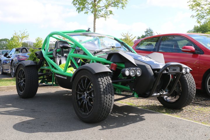 RE: Aston Martin Sunday Service: 8/5/16 - Page 6 - Sunday Service - PistonHeads - The image captures a scene in a parking lot, where several vehicles are parked. Dominating the frame is a striking green and black race car, which features a large windshield and sleek design elements. The car's position suggests it's ready to hit the race track, and its vivid colors make it stand out against the more conventional vehicles surrounding it.