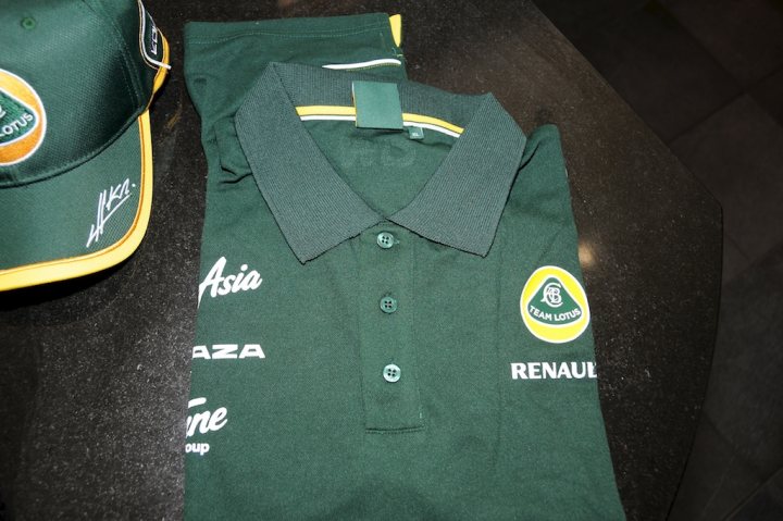 New Team Lotus Gear Turned up today!! - Page 1 - Caterham - PistonHeads - The image showcases a green polo shirt with a number of sponsor logos imprinted across it. The shirt's collar and placket contrast with its main color, adding visual interest. Prominently featured logos include Renault, Delta Airlines, and Aston Martin, suggesting that this shirt might be related to the Aston Martin Racing Team. The shirt appears to be beside a green cap with the same team name, indicating a concerted effort to display the team branding. The overall scene might be set in a retail environment or a fan's collection.