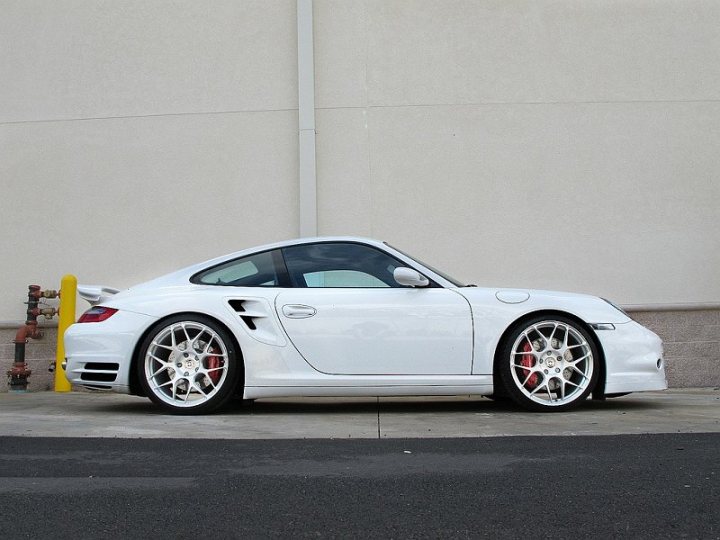 A black and white photo of a car parked in a parking lot - Pistonheads - The image features a white sports car parked next to a yellow pole and a white wall. The car has a sleek design with a black convertible top and black rims, giving it a sporty appearance. The vehicle appears to be well-maintained with shiny exterior paint reflecting its surroundings. The car is parked on an asphalt surface, which suggests the photo might have been taken in a parking lot or a street with parking regulations.