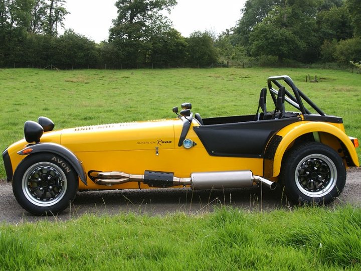 Caterham 620r - what make are the instruments and the wheels - Page 1 - Caterham - PistonHeads - The image showcases a vintage yellow car parked amidst green grass. The car appears to be a convertible with a sleek design, including a drop top and additional wheels on the back, possibly for a rear-wheel drive or unique style. The vehicle displays the name "Aveon" on it, suggesting a past brand association or a custom restoration. It's positioned in a serene, rural setting with trees in the background, providing a scenic contrast to the car's vibrant hue.