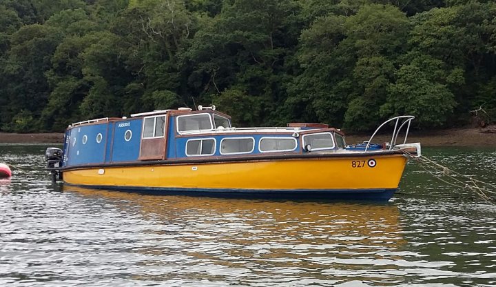 A boat with an interesting history - Page 1 - Boats, Planes & Trains - PistonHeads - The image showcases a boat in motion on a body of water. The boat has a vibrant yellow and blue hull with a subtle curve at the bottom. The top deck is blue, providing a contrast to the yellow hull. The boat offers several windows for cabin light and visibility. In the background, a shore with lush foliage can be seen, suggesting a serene waterfront or perhaps a river alongside a forest. The boat's presence and design suggest it's equipped for leisure or transport, adding to the overall scenic and peaceful atmosphere of the image.