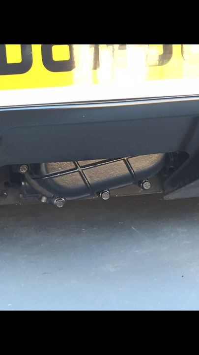 A close up of a car on a city street - Pistonheads - This image displays a close-up view of a vehicle's bumper. Dominating the lower part of the frame is the gray bumper, which features multiple holes and structures. The holes are of varying sizes, suggesting they may be for attaching towing devices or providing sockets for cables. Additionally, the black color contrasts against the gray of the bumper, and there's a yellow line running along the back of the bumper. The focus of the image is on these details, emphasizing the functionality and structure of the bumper.