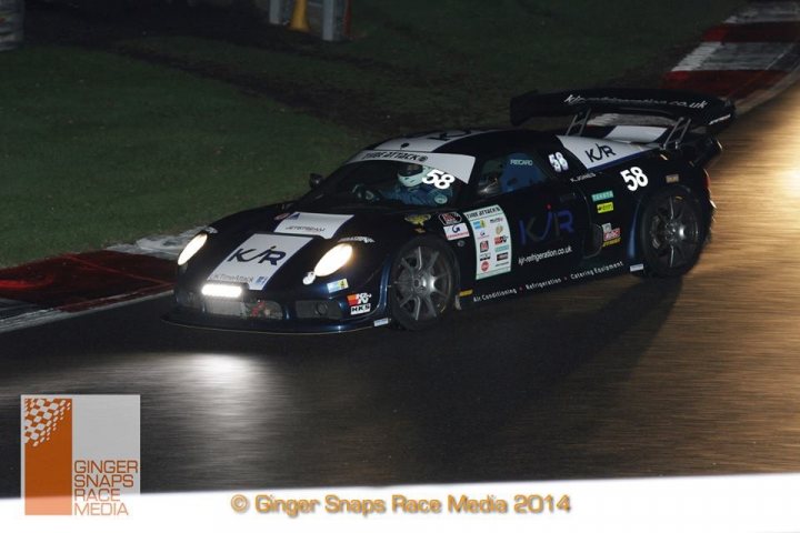 Brands Hatch Timeattack - Page 1 - Noble - PistonHeads - The image captures a dynamic night scene on a race track. The main focus is a race car, with the number 58 prominently displayed on its black exterior. The car is a high-performance KR type, and it appears to be in motion. It's dark, and the car, as seen from the side, is illuminated by its headlights, creating a striking contrast against the black surface of the track. The image is presumably from a media event for Ginger Snaps Race Media, and it's taken in 2014. The logo of the company is at the corner, indicating their involvement in this event.