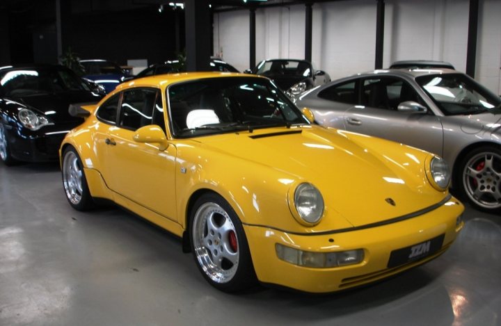 What's your favourite 911? - Page 5 - General Gassing - PistonHeads - This image features a vibrant yellow Porsche parked in a garage amidst other vehicles. The car is positioned in the foreground, demonstrating its distinct design and color. Its polished wheels and front bumper add to its impressive appearance. The garage is spacious, with three additional cars visible in the background, creating a backdrop that accentuates the Porsche's distinctive shape and color. The bright interior lighting contrasts with the enclosure's concrete floor, enhancing the overall visual impact of the scene.