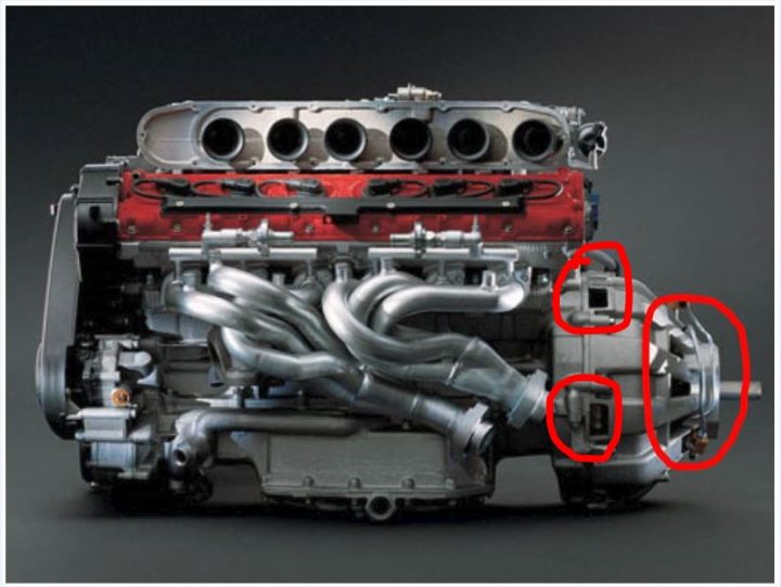 Advice needed, Ferrari 550 Munich area. - Page 1 - Ferrari V12 - PistonHeads - The image features an advanced racing car engine, exhibiting a large grey casing with a red block in the center. The engine is adorned with intricate valve covers, and noticeable red accents. It appears to be mounted on a robust metal frame and is positioned against a stark grey background. Additionally, the perspective of the image accentuates the three-dimensional structure of the engine.