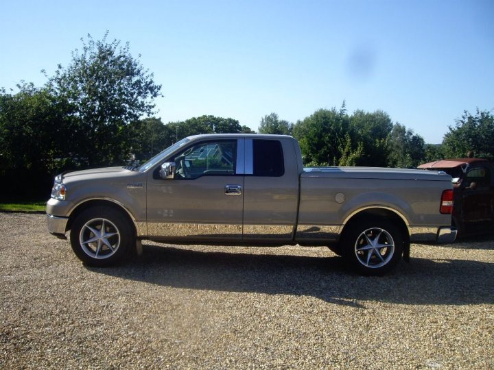 american pickups- what are the like to live with? - Page 12 - General Gassing - PistonHeads - The image shows a silver Ford F150 truck parked on a gravel driveway. The vehicle is positioned at an angle, with the front end and bed visible, highlighting its size and design. The cabin of the truck appears to be doored, suggesting it's either stationary or temporarily unoccupied. In the background, there are trees, indicating a more natural, outdoor setting. The sun is out, casting a soft shadow of the truck on the gravel, providing a serene and undisturbed atmosphere.