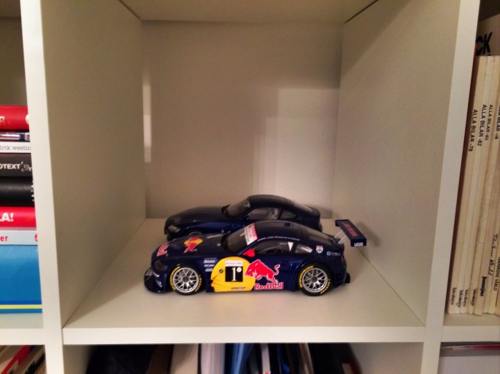 Pics of your models, please! - Page 123 - Scale Models - PistonHeads - The image shows an open bookshelf that is significantly smaller than the rest. The bookshelf is filled with a variety of books, predominantly of the horizontally oriented variety, arranged both vertically and horizontally. On the small shelf, there is a replica of a Red Bull racing car, which stands out due to its vibrant team colors and the unmistakable branding. The design of the bookshelf appears to be designed for compact spaces or to maximize vertical storage, as it is supported by brackets that secure it to the wall.