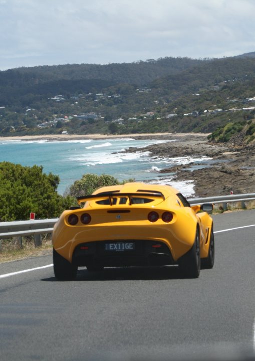 Great Ocean Road - Page 1 - Australia - PistonHeads - In the image, a yellow sports car is driving on a winding road adjacent to the ocean. The car is positioned on the left side of the highway, which curves to the right as it hugs the coastal shoreline. The ocean exhibits multiple ripples as if responding to the sea breezes. On the right side of the road, a guardrail is present, providing a sense of safety while maintaining the eloquence of the natural landscape. The overall scene conveys a sense of motion and adventure, enhanced by the dynamic colors and the harmonious interaction between the man-made vehicle and the natural environment.