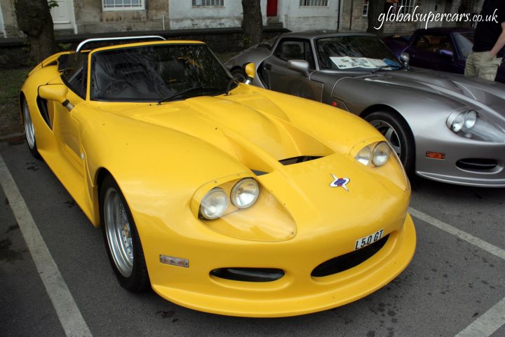 Sunday April 25th Bradford on Avon - Marocs - Page 1 - South West - PistonHeads - The image showcases a vibrant yellow sports car parked on a street amidst other cars. This sports car stands out due to its unique design and distinctive front features. Notably, it has a hood scoop, which is an air intake positioned on the hood. This scoop is intended to increase the flow of ambient air into the engine, enhancing the car's performance. 

It is positioned in a parking lot, suggesting that it is being displayed or utilized for a specific event or purpose. The presence of other cars in the background adds to the bustling ambiance of the scene. Overall, the image captures a moment of a car show or casual gathering of car enthusiasts, where the yellow sports car, with its distinctive features, is a prominent attraction.