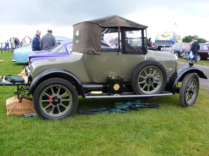 Oulton Park Classic, Performance, Vintage, muscle car show - Page 1 - North West - PistonHeads - The image depicts a vintage car show with classic models on display. An older green truck dominates the scene, taking up a significant portion of the image. The truck's black bed liner appears to be in good condition. The setting is a lush green yard, which suggests the event might be casual and family-friendly. There are a few people milling about in the background, likely admiring the cars and each other. In the far background, more vehicles can be seen, indicating a larger gathering or exhibition.