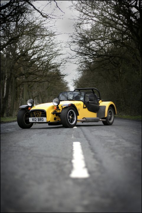 Back in April... - Page 1 - Caterham - PistonHeads - The image presents a striking scene of a vintage sports car occupying a large portion of a tree-lined street. The car, painted with a bold silver and black color scheme, is a two-door model with a sleek design that angles back at the hood and tapers towards the front. The vehicle is parked in a manner that leaves its hood open, which contrasts with the relatively normal setting of a peaceful, tree-enveloped road. The road itself seems to be set in a scenic, forest-like environment, adding to the tranquility and solitude of the scene. The presence of the parked car in the wilderness evokes a sense of adventure and escape from the hustle and bustle of everyday life.