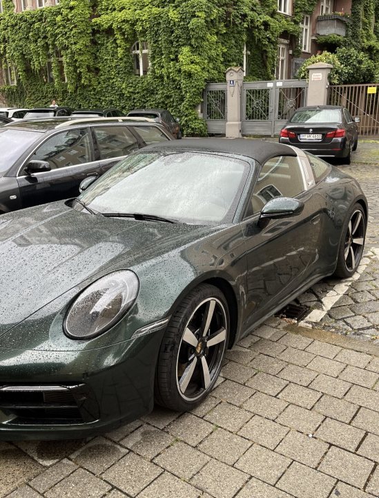 misbadging cars - Page 200 - General Gassing - PistonHeads UK - The image shows a dark green Porsche sports car parked on the side of a street. It has a sleek design with a sloping roofline and wide rear fenders, which are characteristic of many modern Porsche models. The car is positioned next to the curb and appears to be wet, suggesting it might have recently rained or the street is damp. There is a building in the background, partially obscured by trees. To the left of the image, there's a parking lot with several cars visible. The photo has a watermark text across it that reads "COPYRIGHT: 2018-07-23